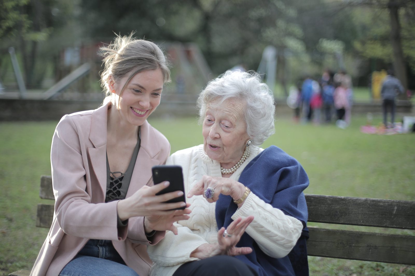 A woman showing her grandmother something on a phone while sitting together on a park bench